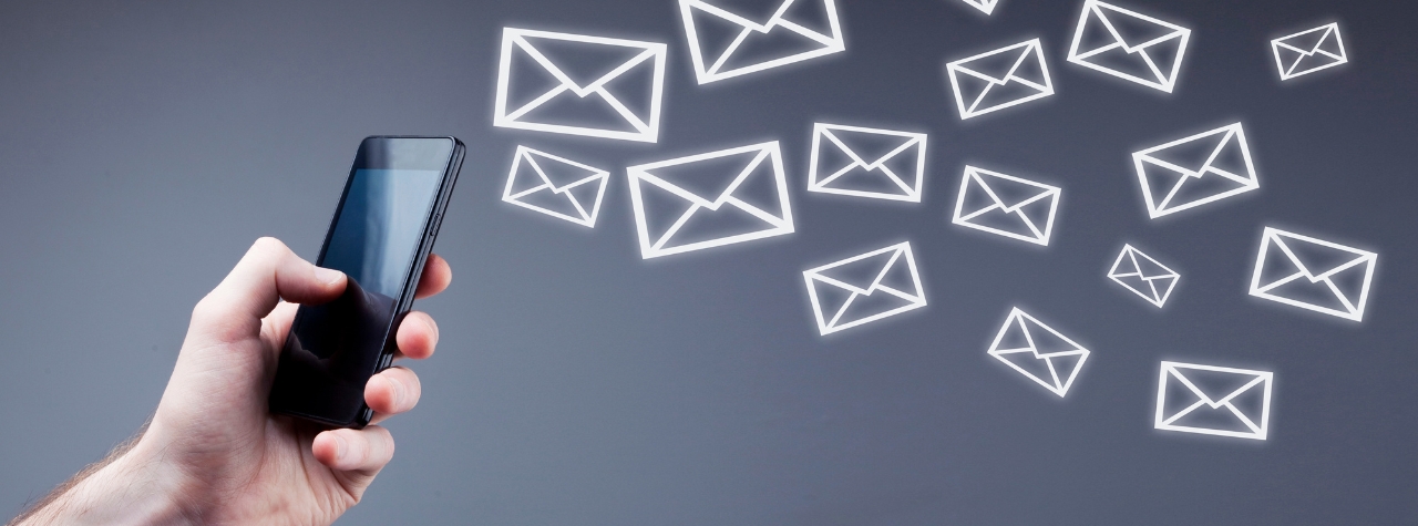 A hand holding a cellphone on the left side of the image. Many text message icons are flying out of the phone.