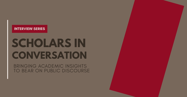 A plain brown background with a red vertical strip on the right. There is the text of the left saying: Interview series Scholars in Conversation - Bringing academic insights to bear on public discourse