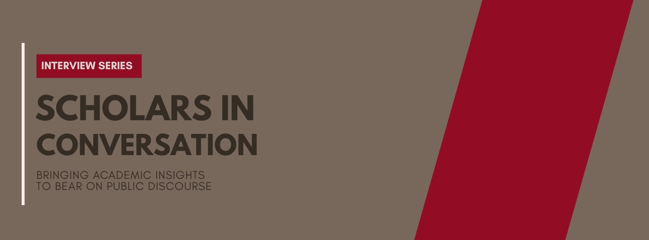 A plain brown background with a red vertical strip on the right. There is the text of the left saying: Interview series Scholars in Conversation - Bringing academic insights to bear on public discourse