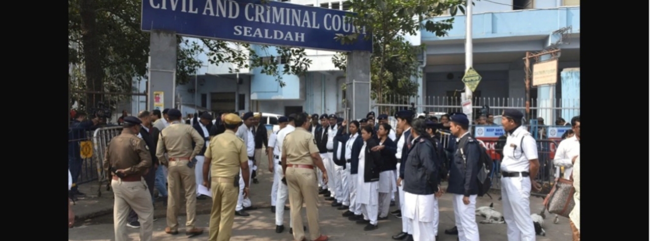 Image showing a group of uniformed police officers, court officers, and lawyers stand gathered outside the entrance of a building marked “Civil and Criminal Court, Sealdah.” Security barricades are visible near the gate.