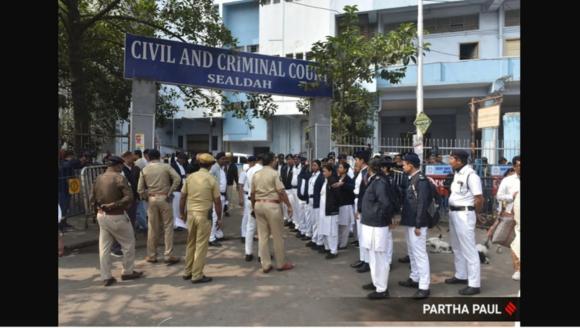 A group of uniformed police officers, court officers, and lawyers stand gathered outside the entrance of a building marked “Civil and Criminal Court, Sealdah.” Security barricades are visible near the gate.