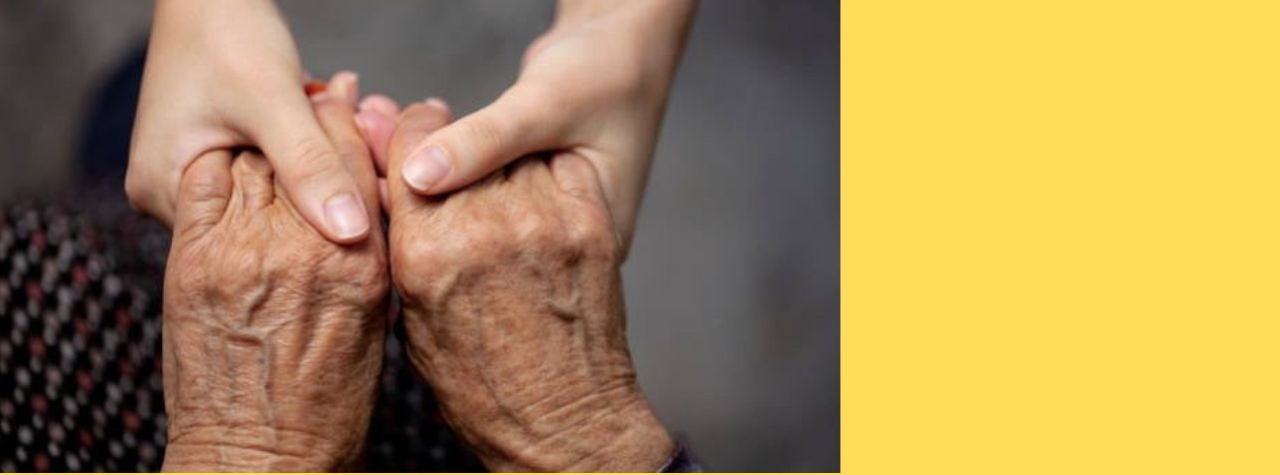 A photo of an old person’s wrinkled hands being gently held by a younger person’s hands.